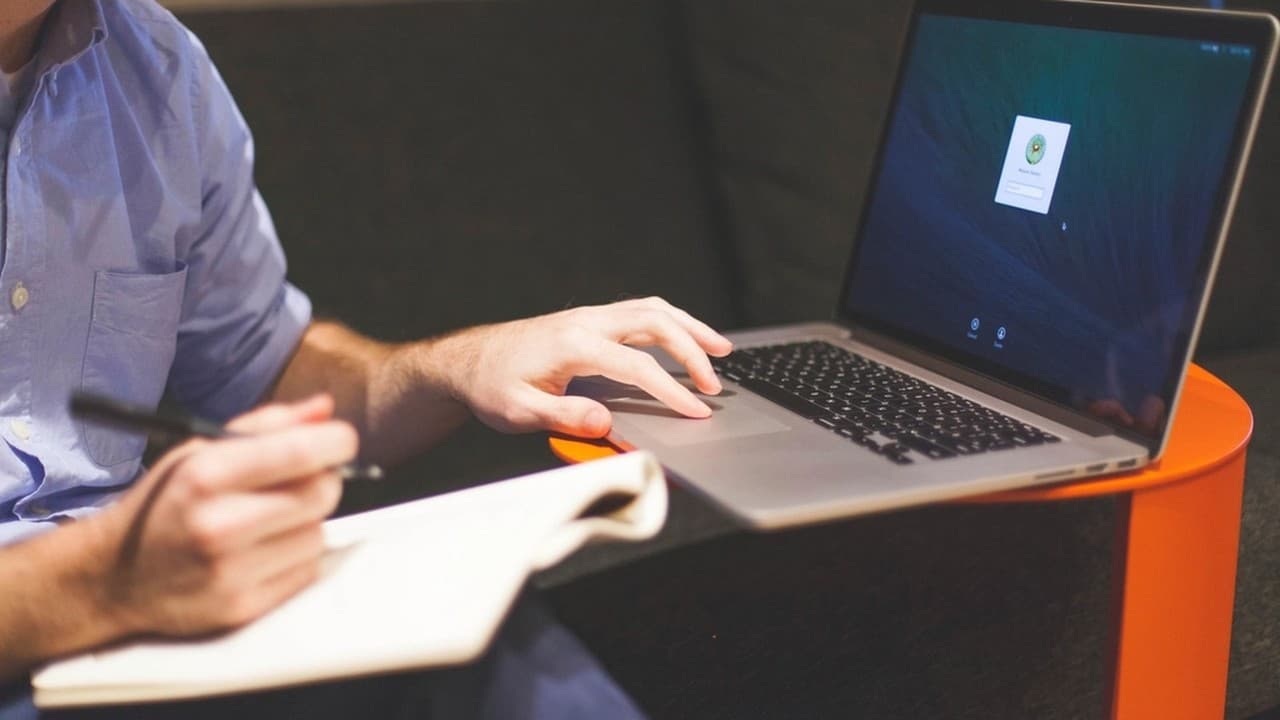 Man typing on a laptop while taking notes